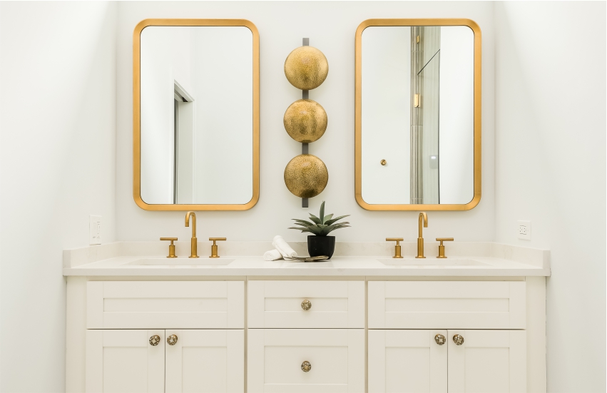 A white bathroom with two gold mirrors.