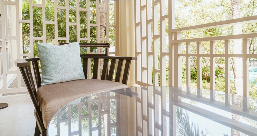 A chair and table on a balcony overlooking a tropical garden.