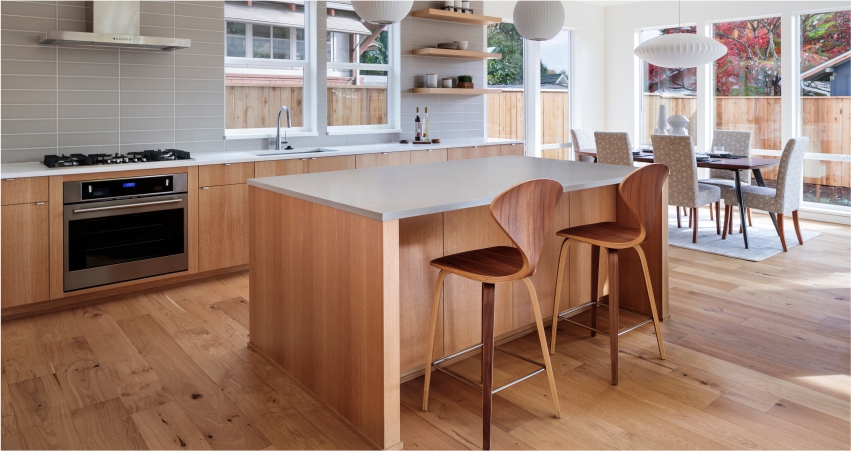 Modern open kitchen interior with wooden finishes and a dining area in the background.