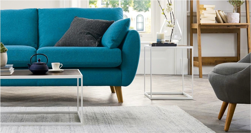 A living room with a blue sofa, coffee table and windows to optimise the entry of natural light.