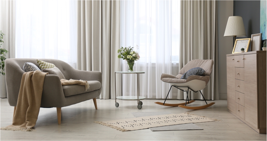 A living room with a rocking chair, beautiful light curtains and a lamp.