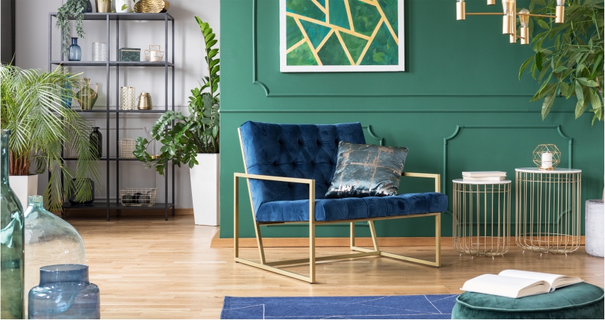A living room with green walls, a blue velvet chair and properly organized corner areas for storage.