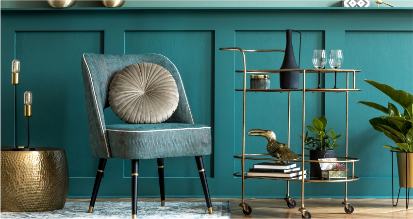 A living room with teal walls and a gold bar cart.