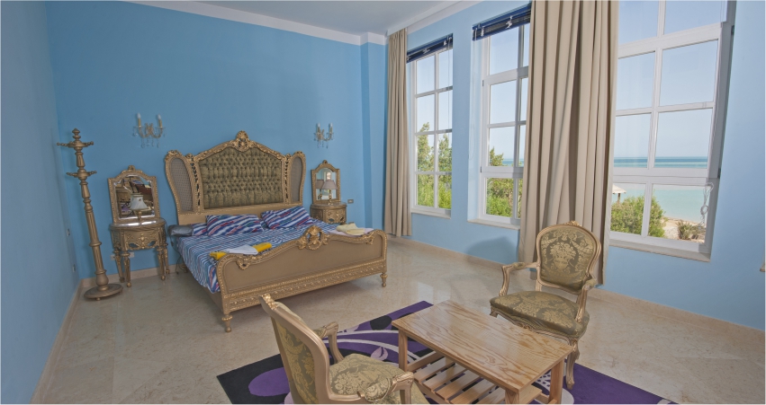 A blue bedroom with an ornate bed, a view of the ocean and shiny sea gold texture design wall.