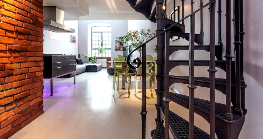 A spiral metal staircase leading to a room with a brick wall.