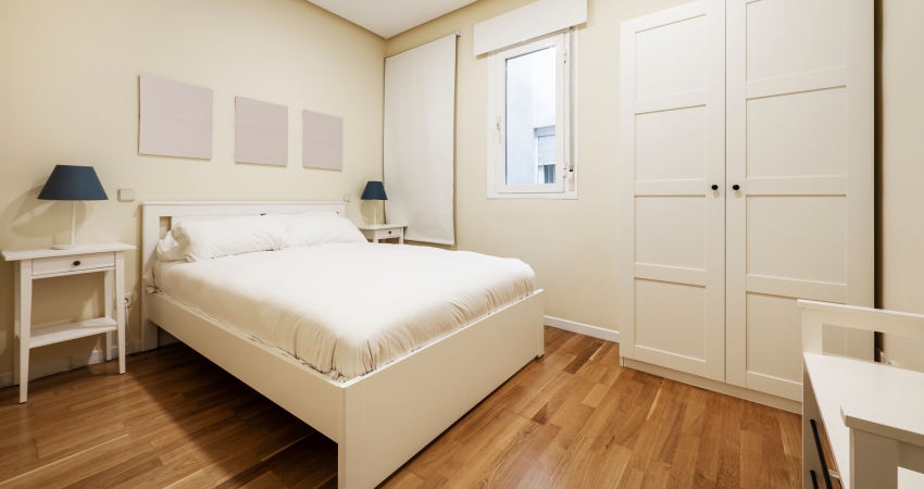 A white bedroom with oak wooden floors and a white bed.