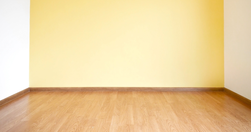 An empty room with a yellow wall and wooden floor.