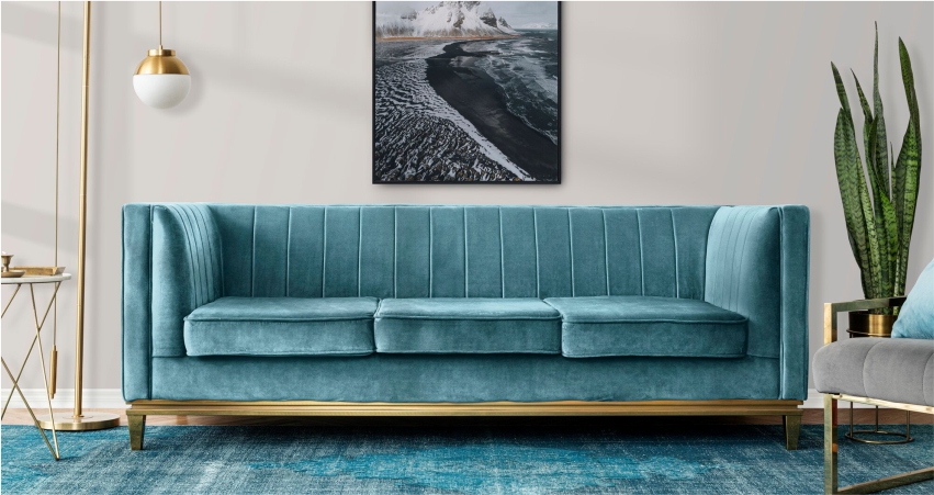 A blue velvet sofa in a living room with a painting on the wall.