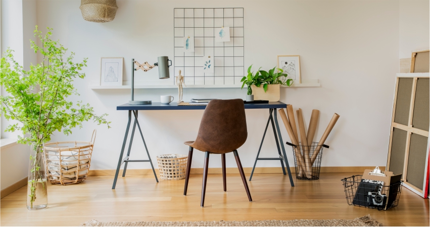 A room with a study desk, chair and a plant.