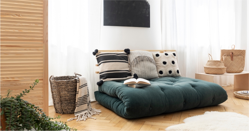 A living room with a green couch and pillows in corner.