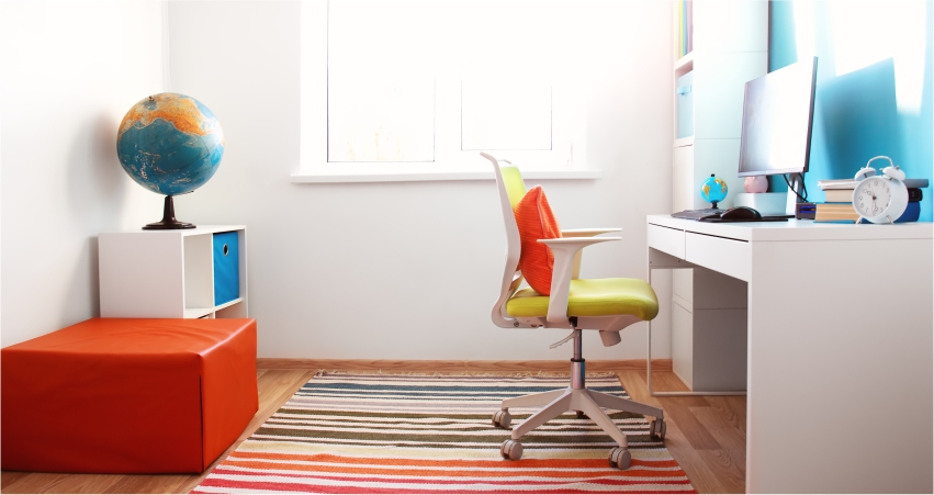 A child's room with a desk, chair and colorful rug.