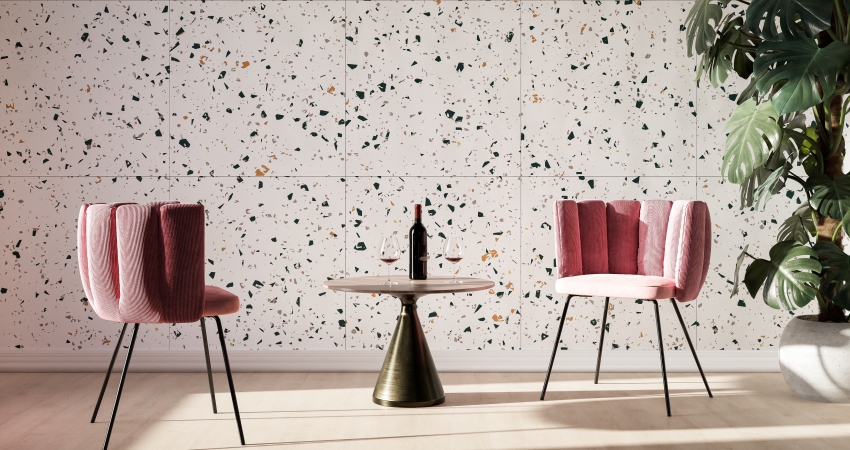 Two pink chairs and a table in front of a speckled wall with designer wall tiles.