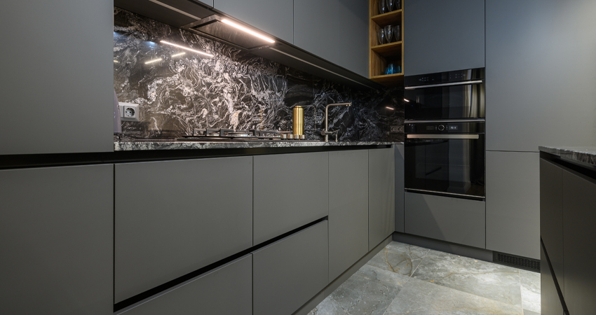 A modern kitchen with grey cabinets and marble counter tops.