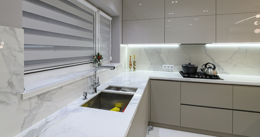 A white kitchen with marble counter tops and a sink.