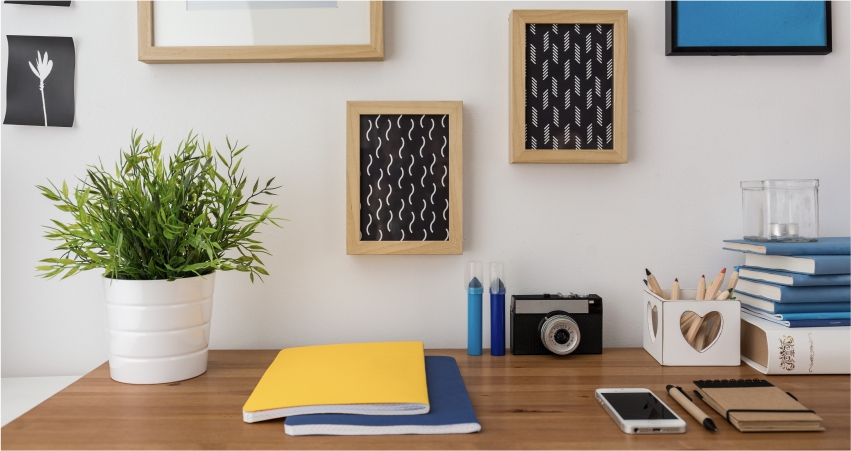 A desk with framed pictures, a plant and a notebook.