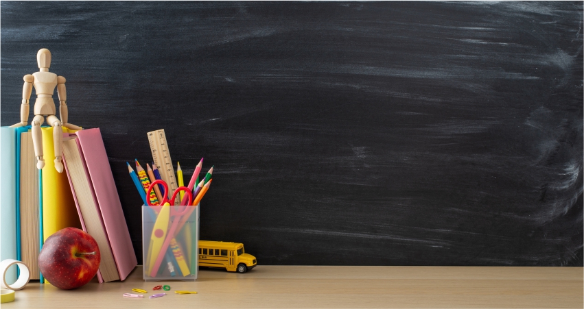 School supplies on a table with a blackboard in the background.