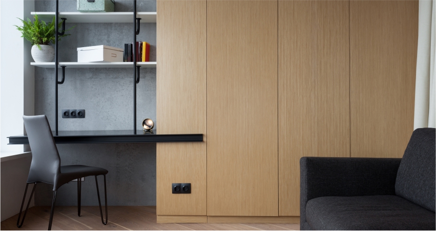 A room with a desk, wardrobe, chair and shelves.