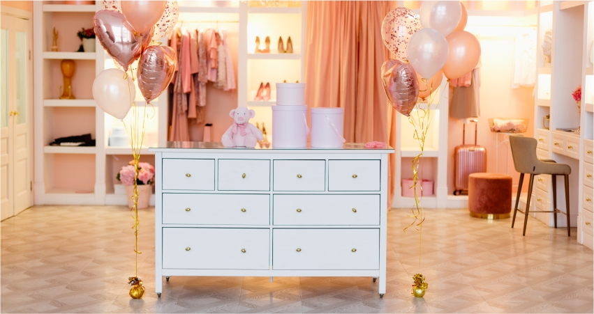 A festively decorated room with a white dresser, helium balloons, and a pastel color scheme.