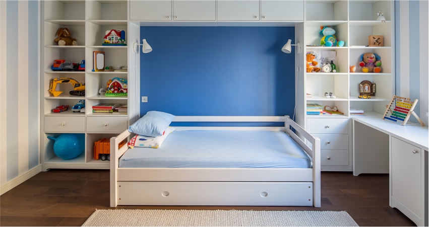 A neatly organized child's bedroom with a white bed, blue accent wall, and shelves filled with toys and books.