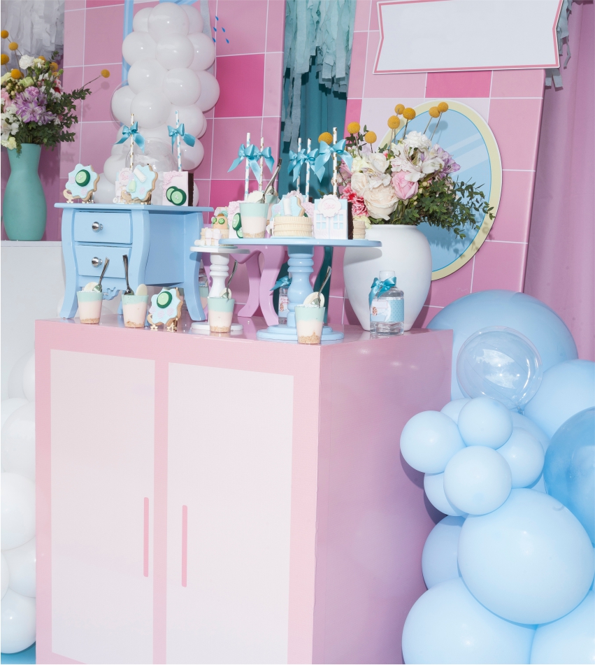 A pastel-colored party setup with balloons, flowers, and themed decorations on a table and a dresser.