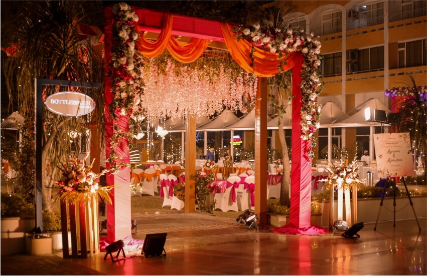 Beautifully decorated outdoor wedding entrance with floral arch, drapes, and warm lighting. 