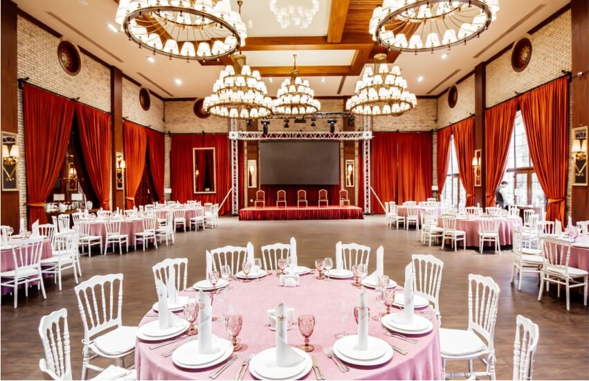 Elegant wedding banquet hall red drapes, beautifully set tables, and polished wooden flooring.