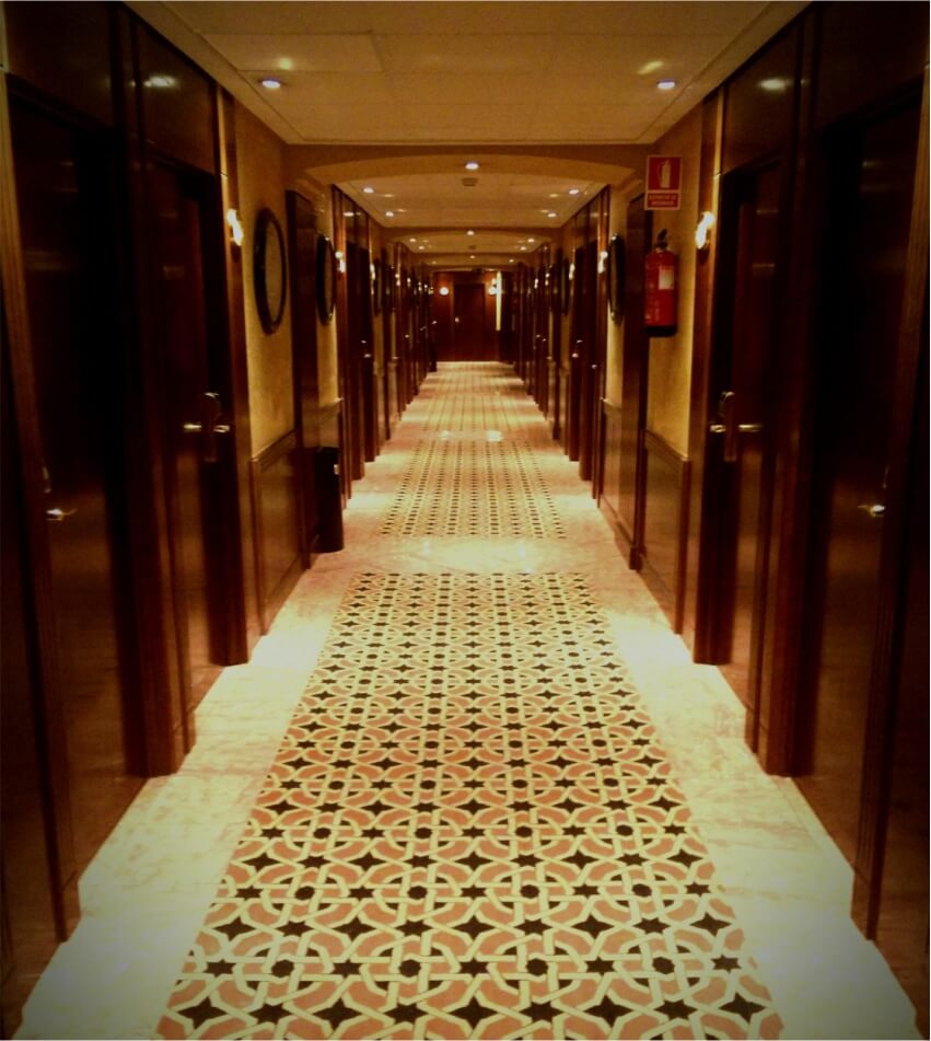 Elegant hotel corridor with warm lighting, wooden doors, and intricate patterned tile flooring 