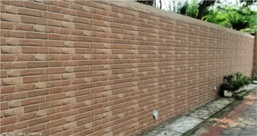 A long outdoor wall covered with cement tiles in a brick pattern with potted plants nearby